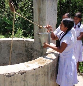 Een meisje haalt water uit een waterput in Sri Lanka.
