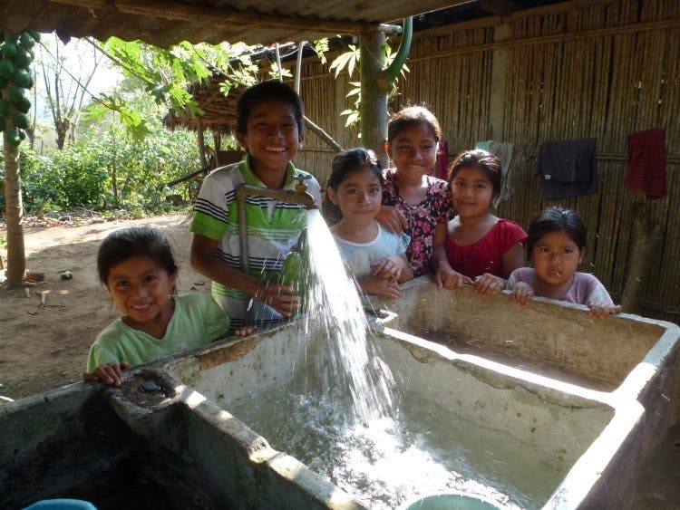Zes blije kinderen bij een nieuwe kraan met drinkwater in Guatemala.