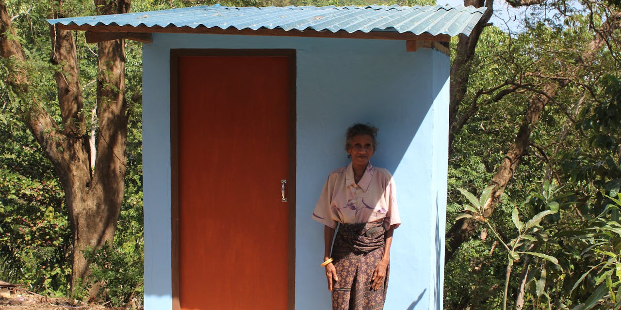 Een oudere vrouw poseert bij een nieuwe wc in Indonesië.