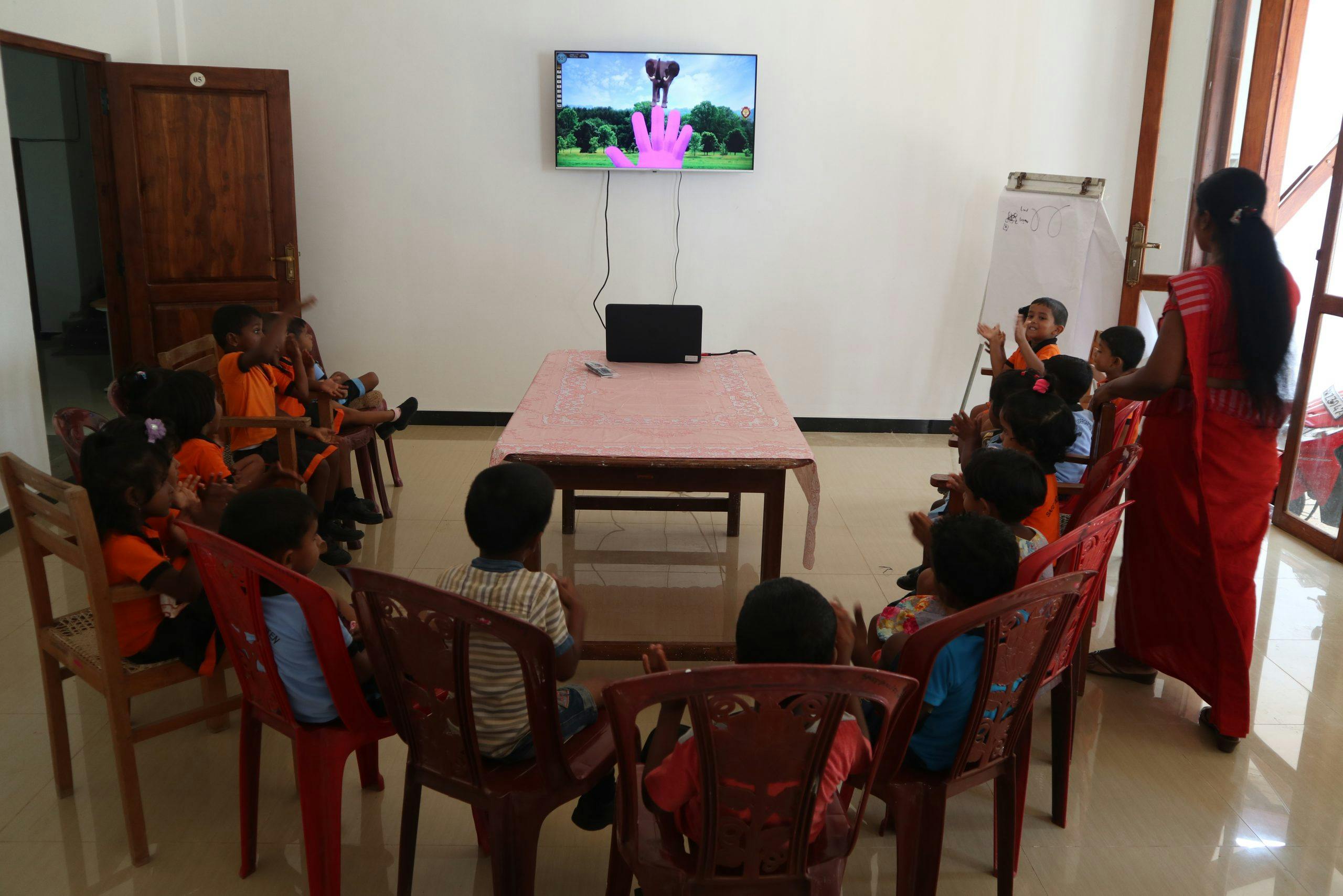 Basisschoolkinderen zitten in een halve cirkel voor een tv op school in Sri Lanka.
