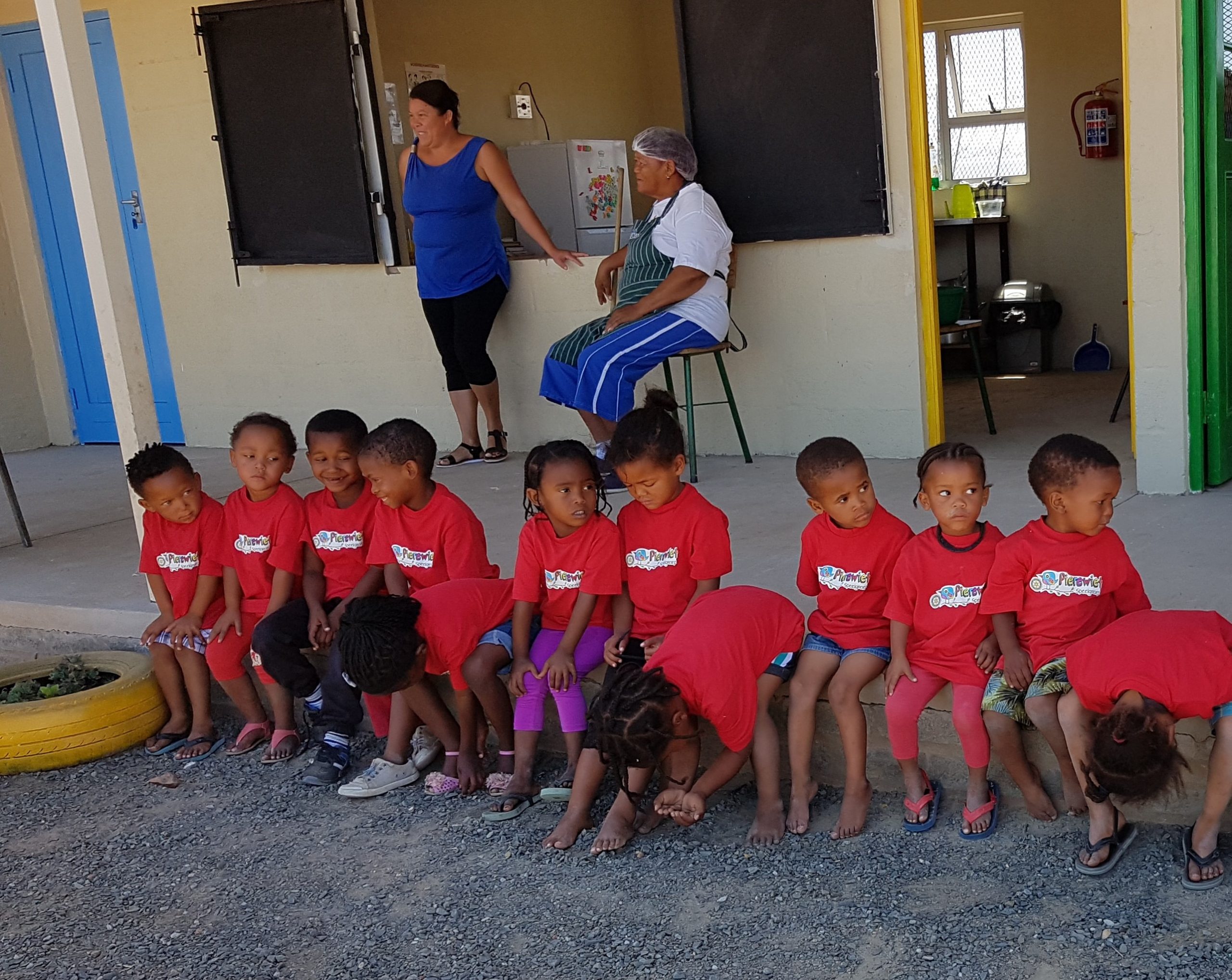 Een rij kinderen met rode shirts zit op de stoep van hun school.