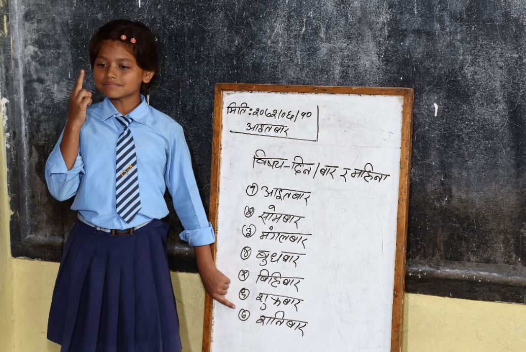 Een meisje staat naast een lesbord op een dovenschool in Nepal.
