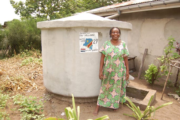 Een vrouw staat voor een betonnen watertank in Congo.