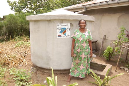 Een vrouw staat voor een betonnen watertank in Congo.