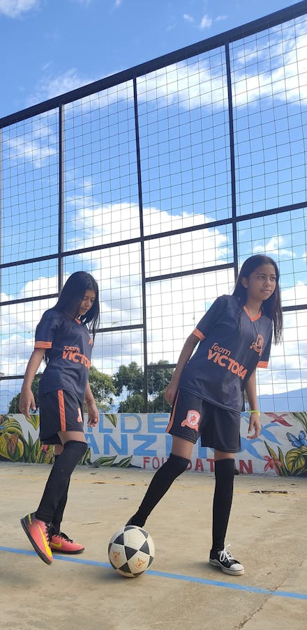 2 meisjes met voetbalshirts en bal op een straatvoetbalveldje in Colombia.