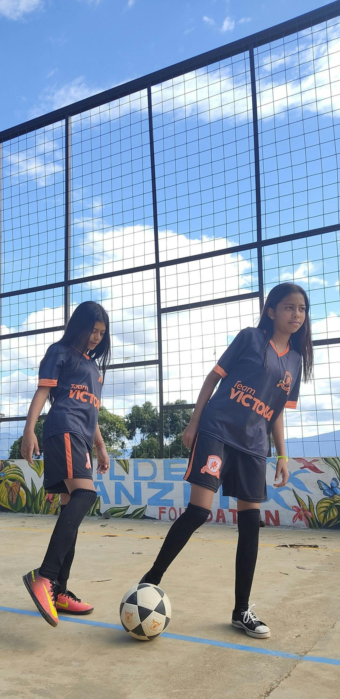 2 meisjes met voetbalshirts en bal op een straatvoetbalveldje in Colombia.