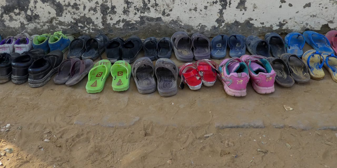 Twee rijen kinderschoenen staan tegen een muur bij een school in India.