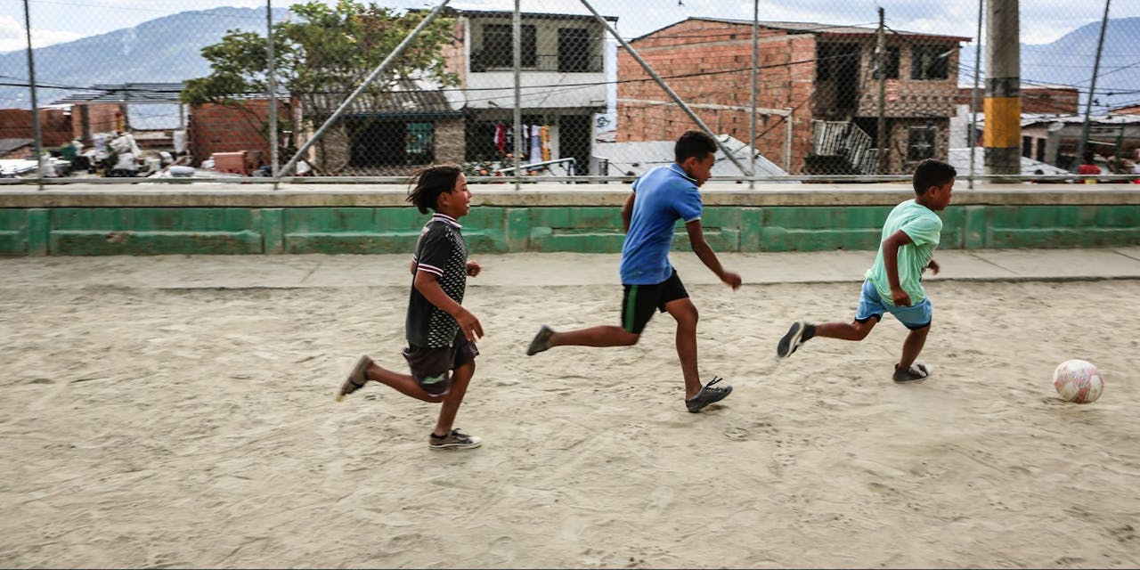 Drie straatkinderen voetballen op een pleintje in Colombia.