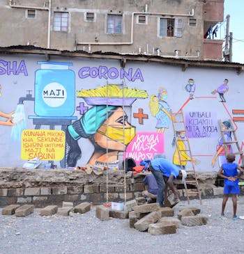 Twee kinderen kijken naar een muurschildering die waarschuwt tegen corona. Een jongerencentrum is hard nodig in de strijd tegen werkloosheid.