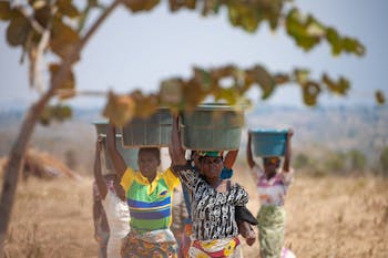 Drie vrouwen in Malawi lopen met de graanoogst in manden op hun hoofd.