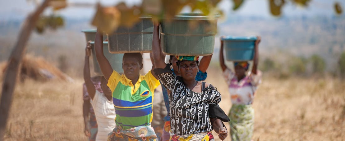 Drie vrouwen in Malawi lopen met de graanoogst in manden op hun hoofd.