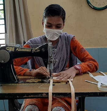 Een meisje met een mondkapje aan het werk achter een naaimachine in India.