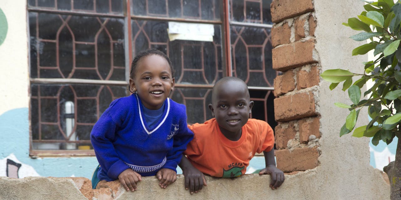 Twee kinderen hangen over de muur van hun school in Oeganda.