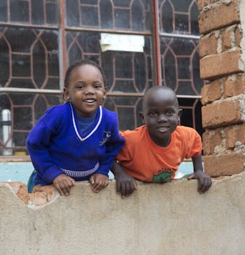 Twee kinderen hangen over de muur van hun school in Oeganda.