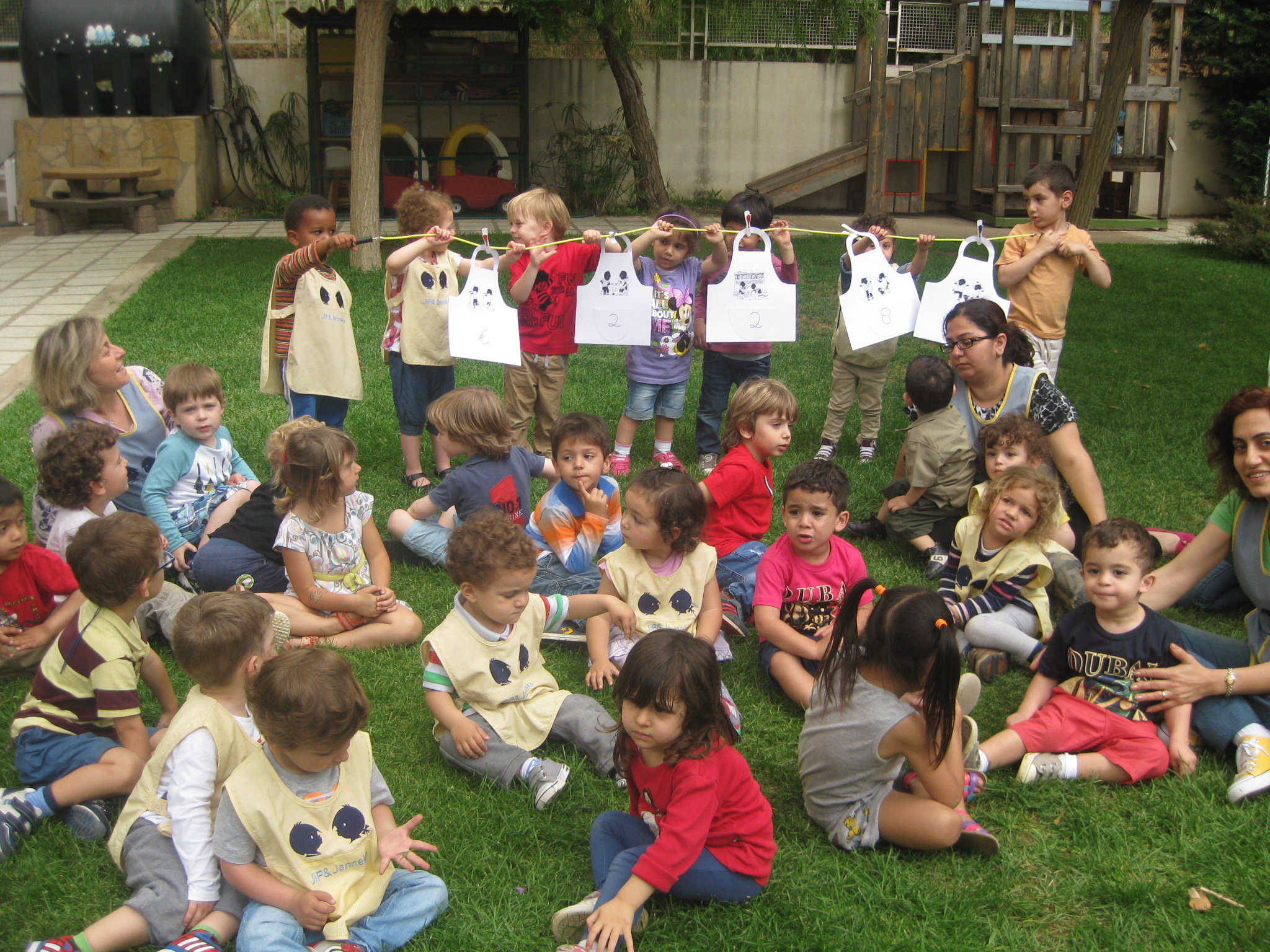 Een groep kleine kinderen zit op een grasveld, buiten hun school in Libanon.