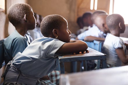 Een groepje kinderen kijkt leunend op hun tafeltjes naar het bord in hun klas.