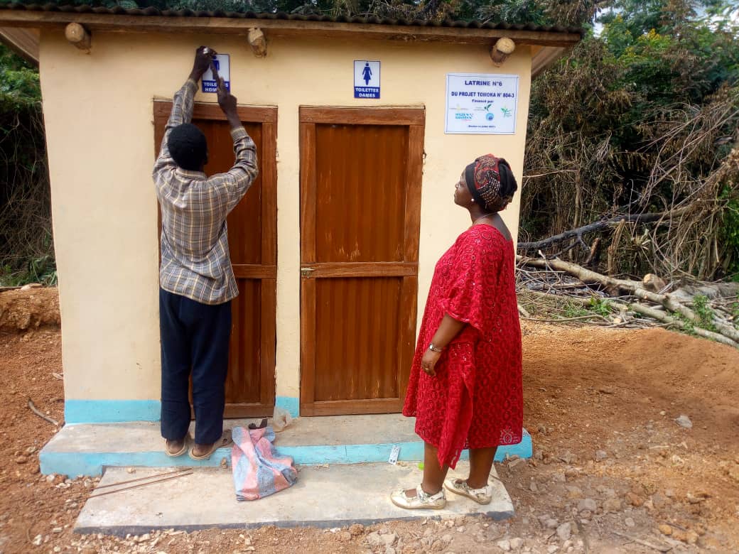 Een man en een vrouw leggen de laatste hand aan een nieuw toiletgebouw in Togo.