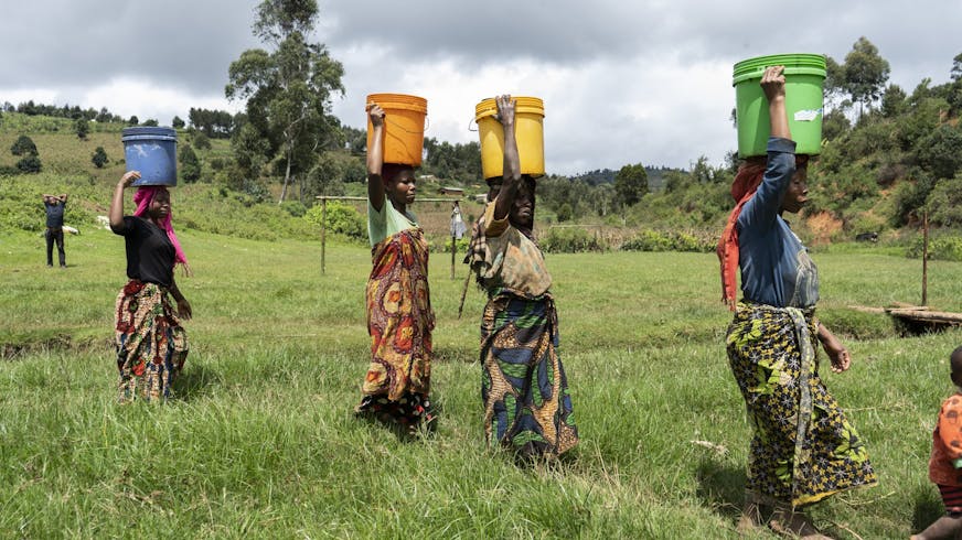 Vier vrouwen lopen met emmers water op hun hoofd.