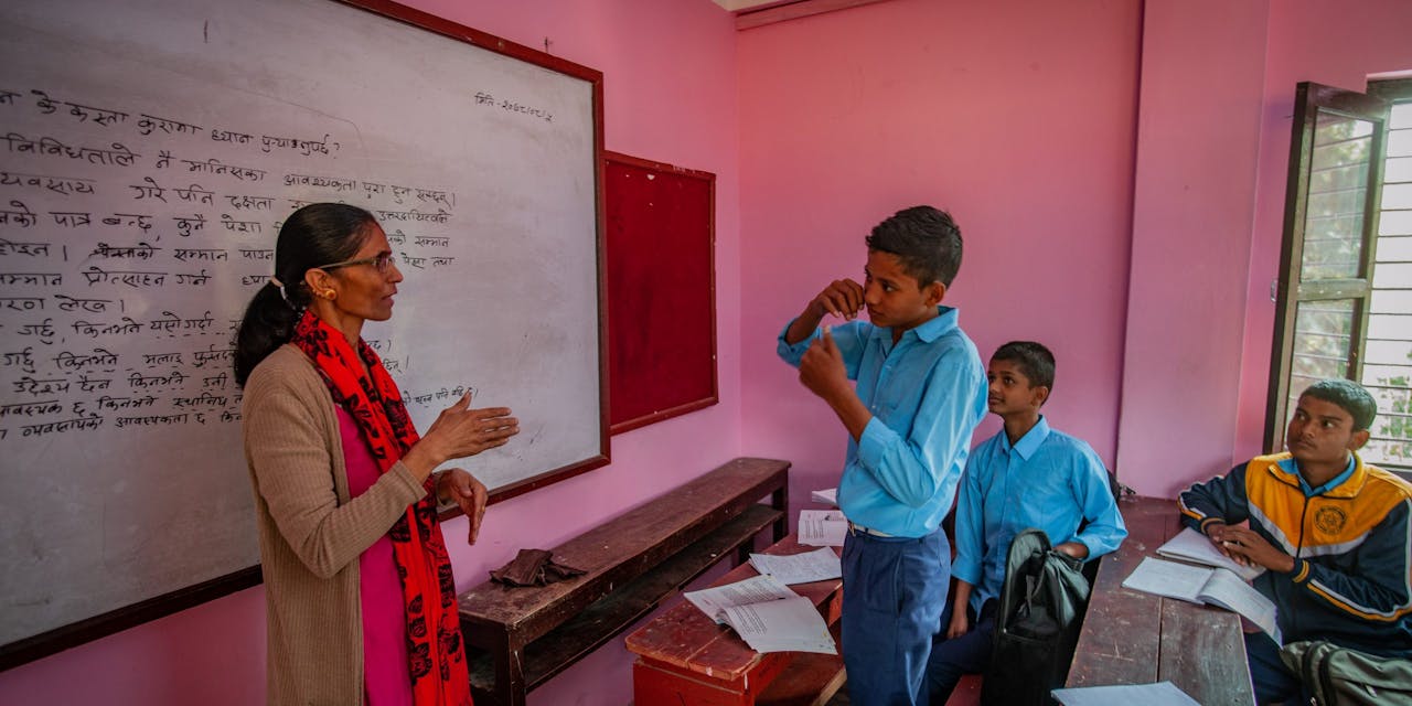 Een roze klaslokaal met leerlingen en een docent in Nepal.