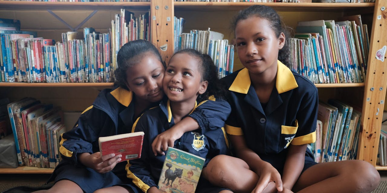 Drie meisjes met boeken in een bibliotheek in Zuid Afrika.