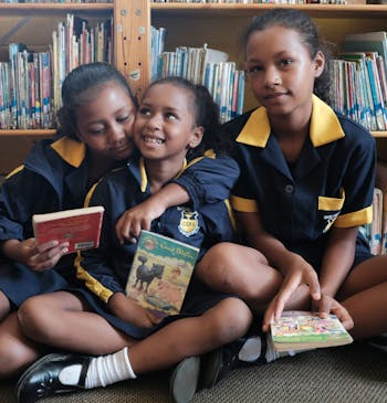 Drie meisjes met boeken in een bibliotheek in Zuid Afrika.