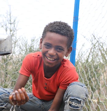 Een lachend jongetje vangt water op uit een buitenkraan in Ethiopië.