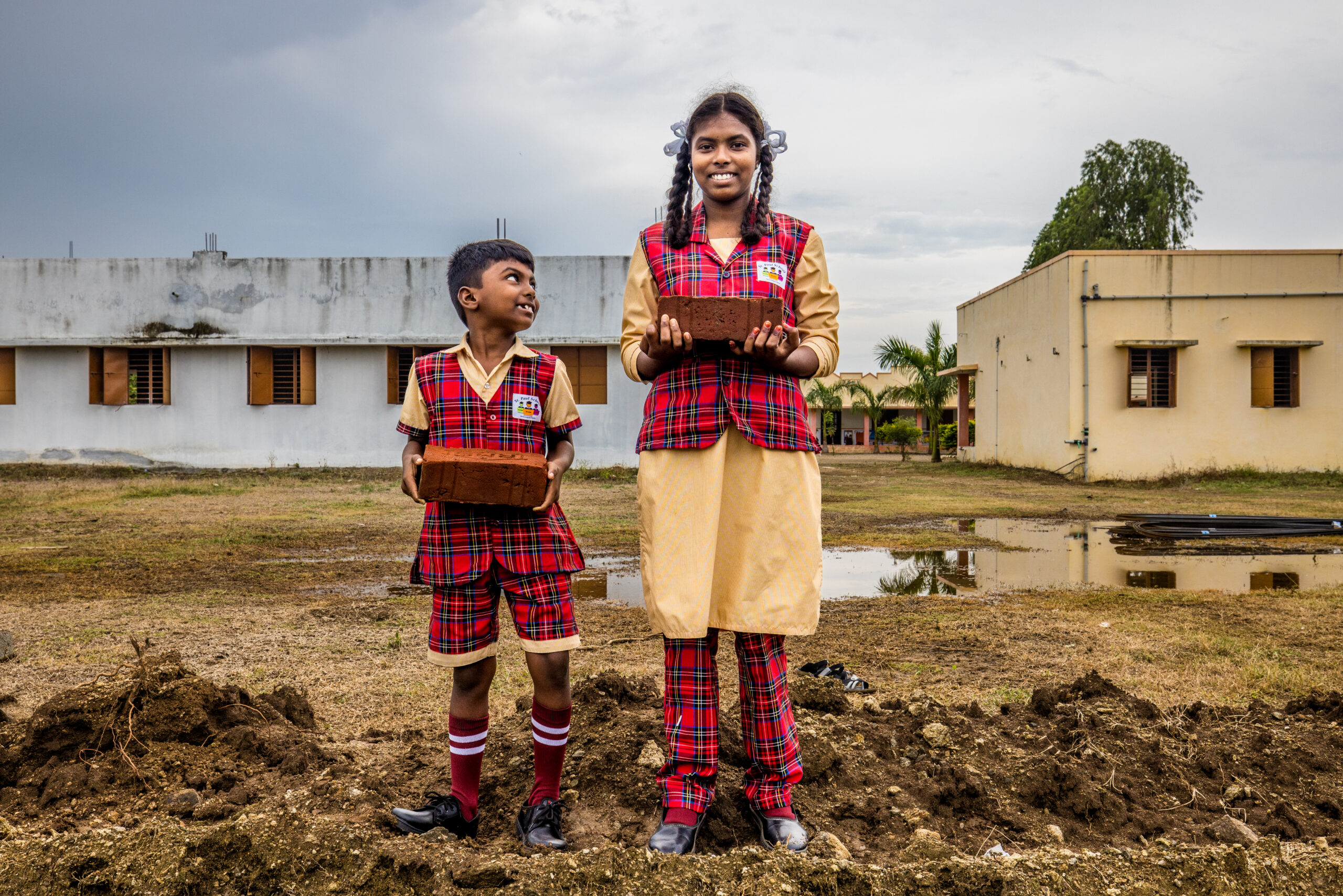 Twee kinderen in india leggen de eerste steen van een muur voor hun school.