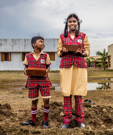 Twee kinderen in india leggen de eerste steen van een muur voor hun school.