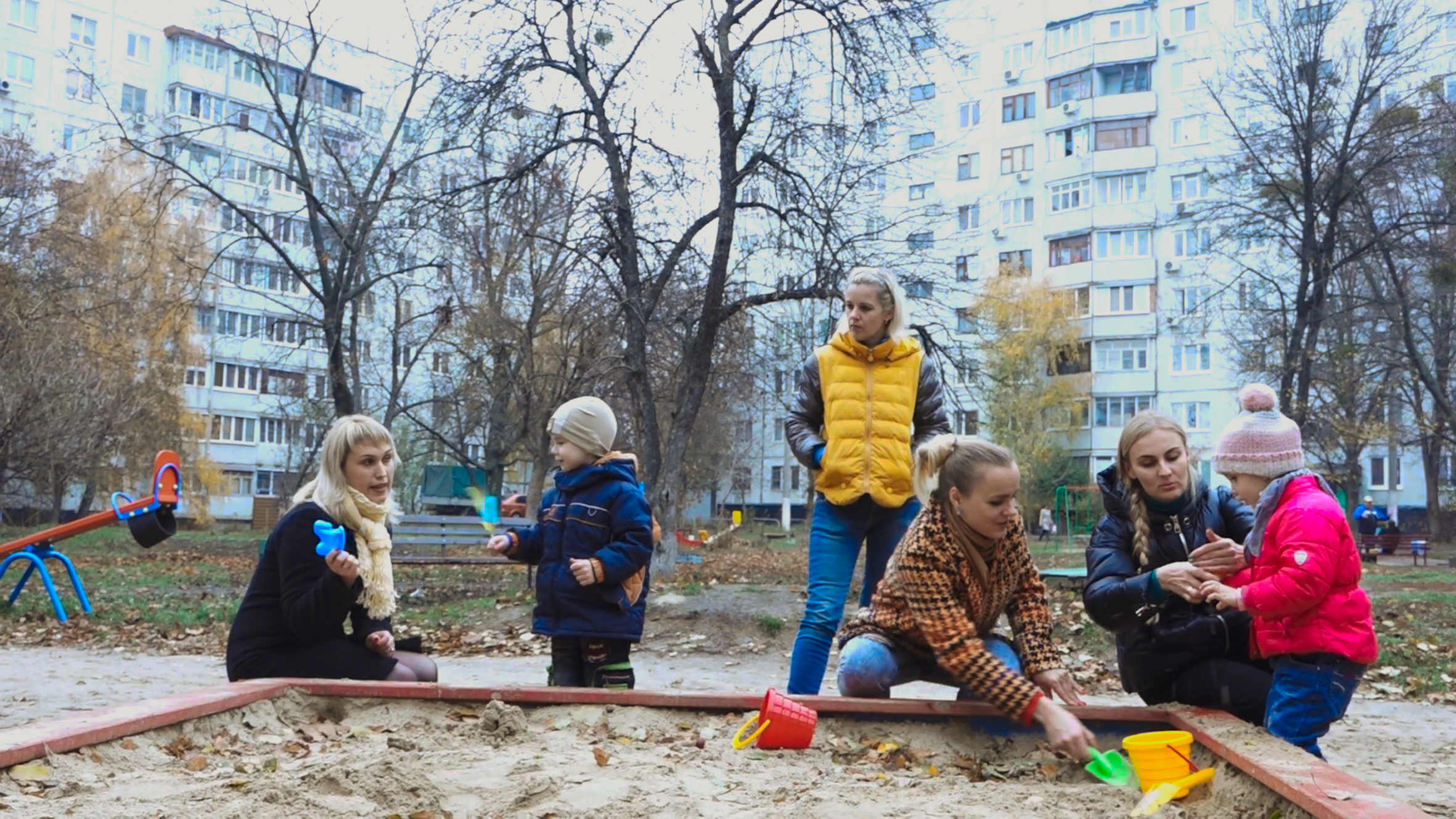 Een groep kinderen met hun moeders in een zandbak in Oekraïne.