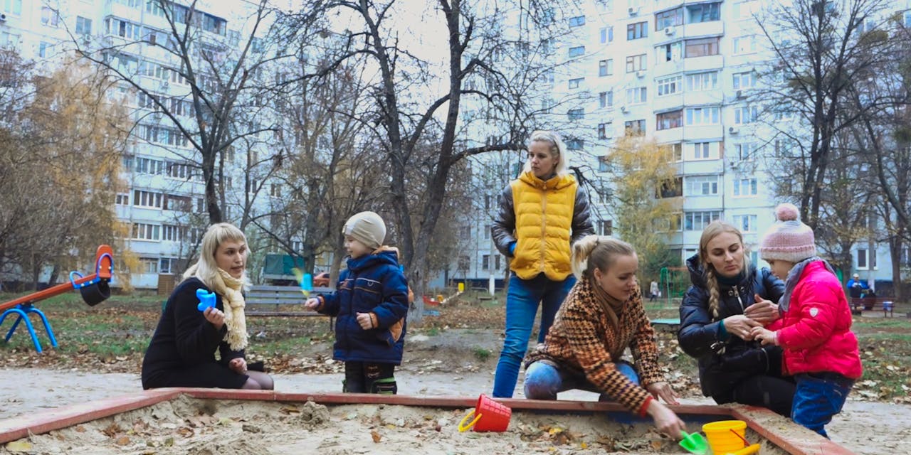 Een groep kinderen met hun moeders in een zandbak in Oekraïne.