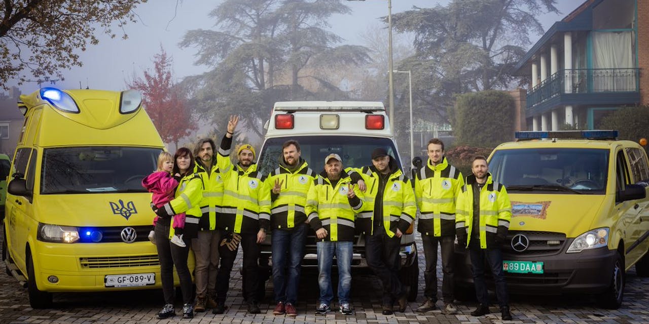 Een groep zorgverleners bij gedoneerde ambulances voor Oekraïne.