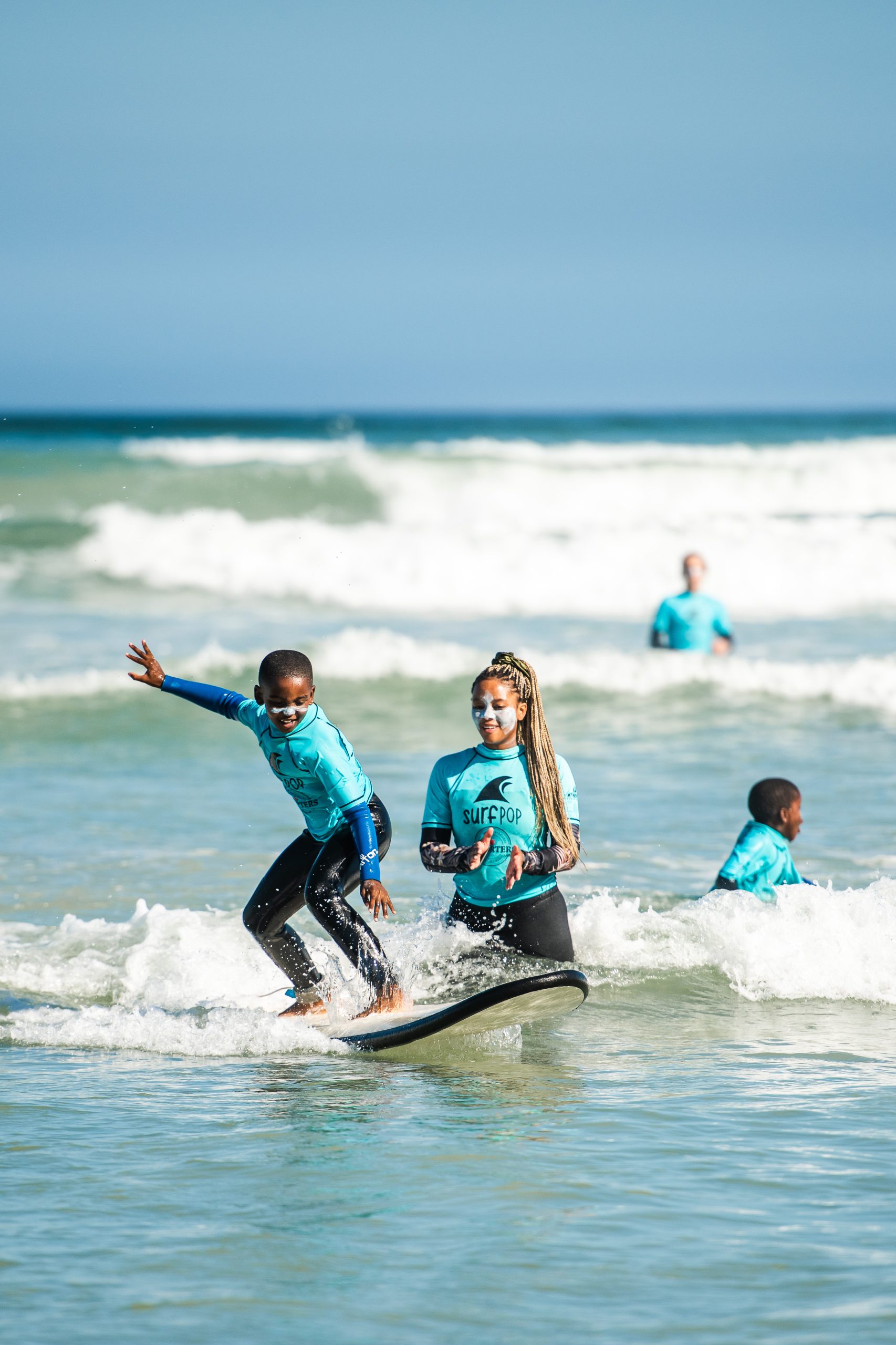 Kind op surfplank met surfdocent erachter.