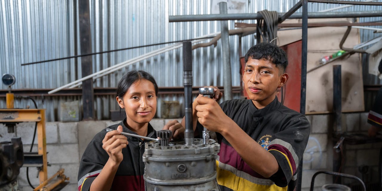 Guatemala-2022.0282 Twee studenten van een vakschool in Guatemala sleutelen aan een auto onderdeel.