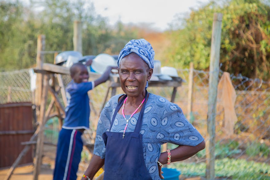 Een vrouw staat bij een moestuin met een jonge jongen op de achtergrond.