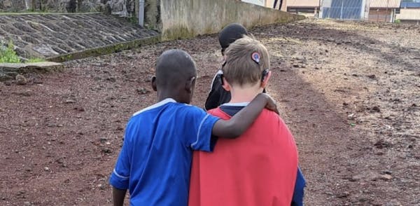 Twee jongens lopen naast elkaar, een heeft de arm om de andere jongen heengeslagen.