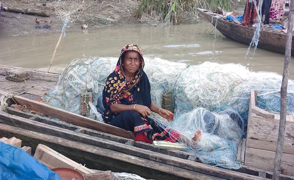 Een vrouw op een visserbootje met visnetten naast zich.