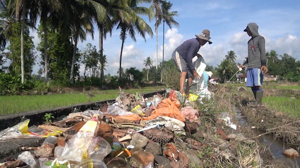 Twee mensen staan in een rivier gevuld met plastic afval.