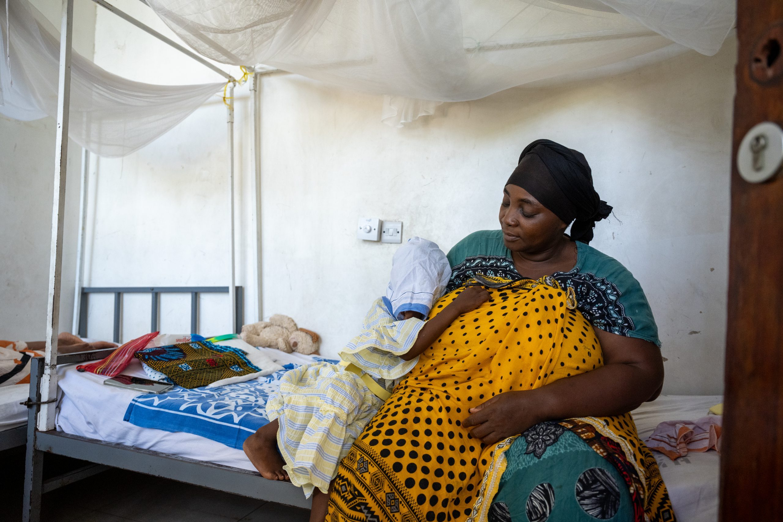 Een vrouw zit met een kind op een ziekenhuisbed.